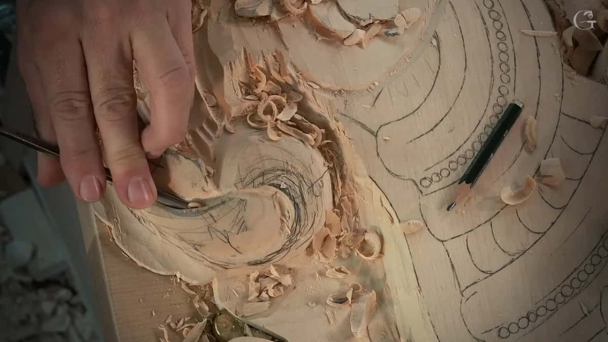 Small veiner held in the fingertips at the acanthus eye, a pencil lying on the uncarved half of the board