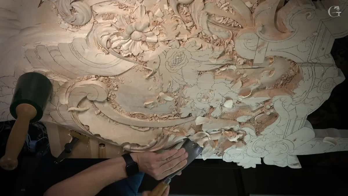 Mallet lying beside a big chisel on the wide carved panel, chips over everything