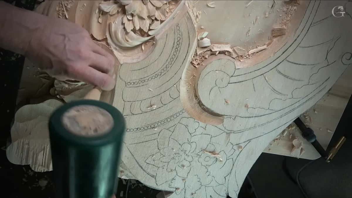 Green mallet resting in the foreground while the other hand steadies a panel still covered in pencil design lines