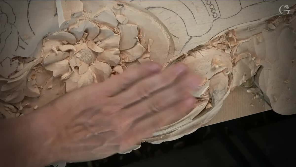 An open palm laid flat across the carved section, shavings lying all around the flower beside it