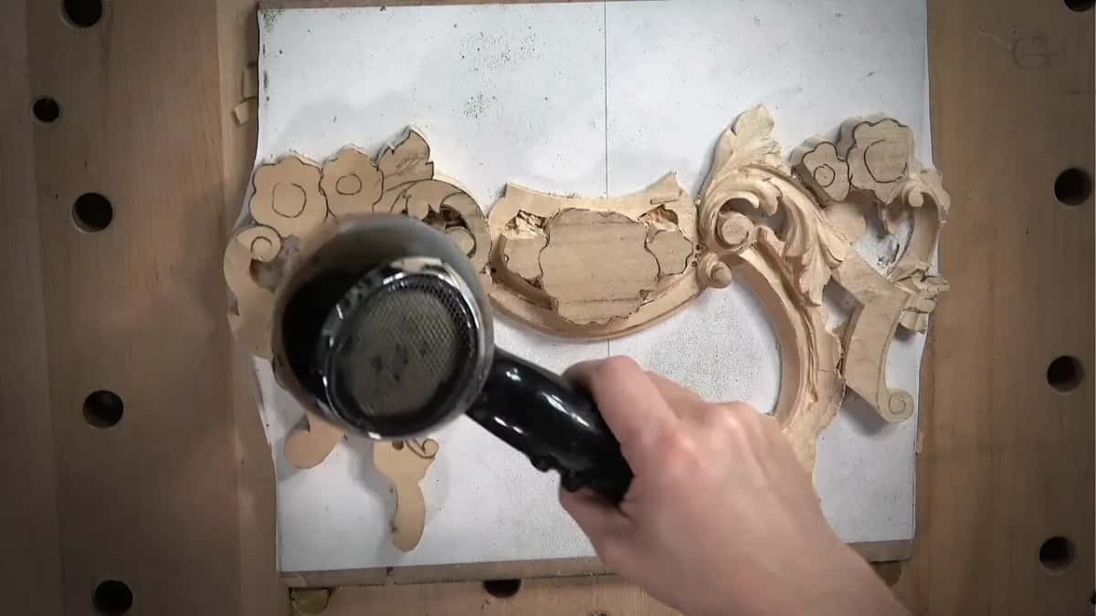 A hair dryer held over a floral carving on a white board