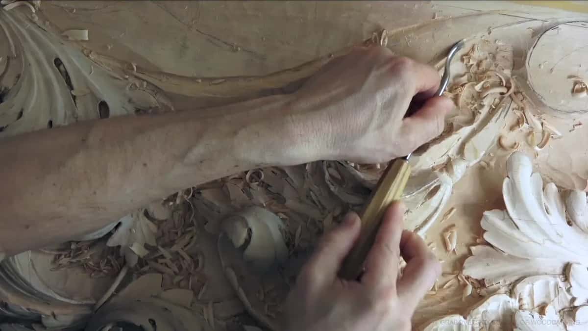 Across the molding band, a hooked blade on a yellow handle, the arm reaching over from the left.
