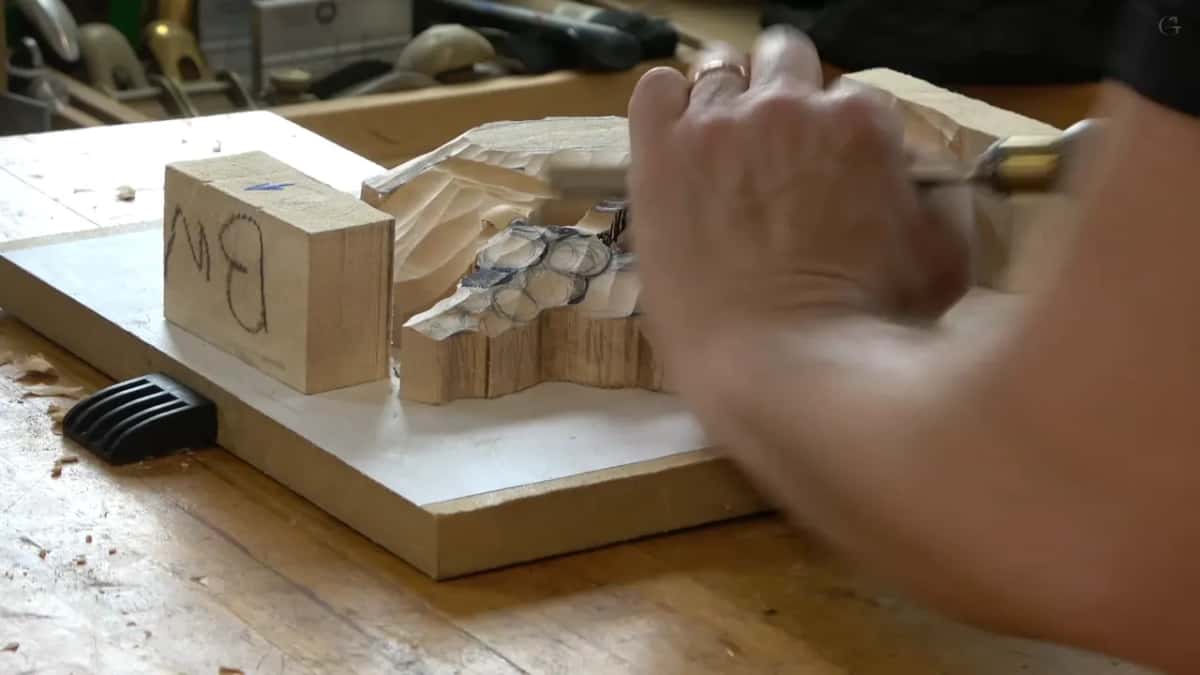 Hand steadying the panel on its backer board while a gouge works into the group of small blooms