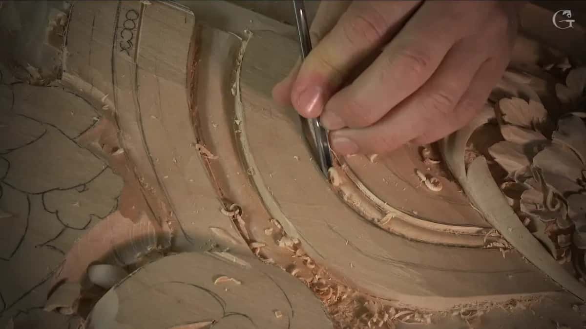 Slim gouge standing in the curved groove while fingers pinch the blade low, close to the wood surface
