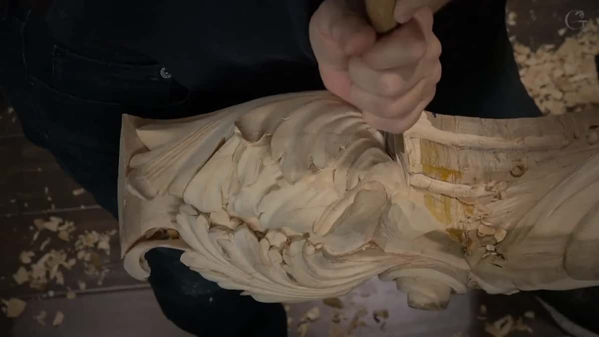 A closed fist on the handle presses the blade into the marked wood beside the leaves.