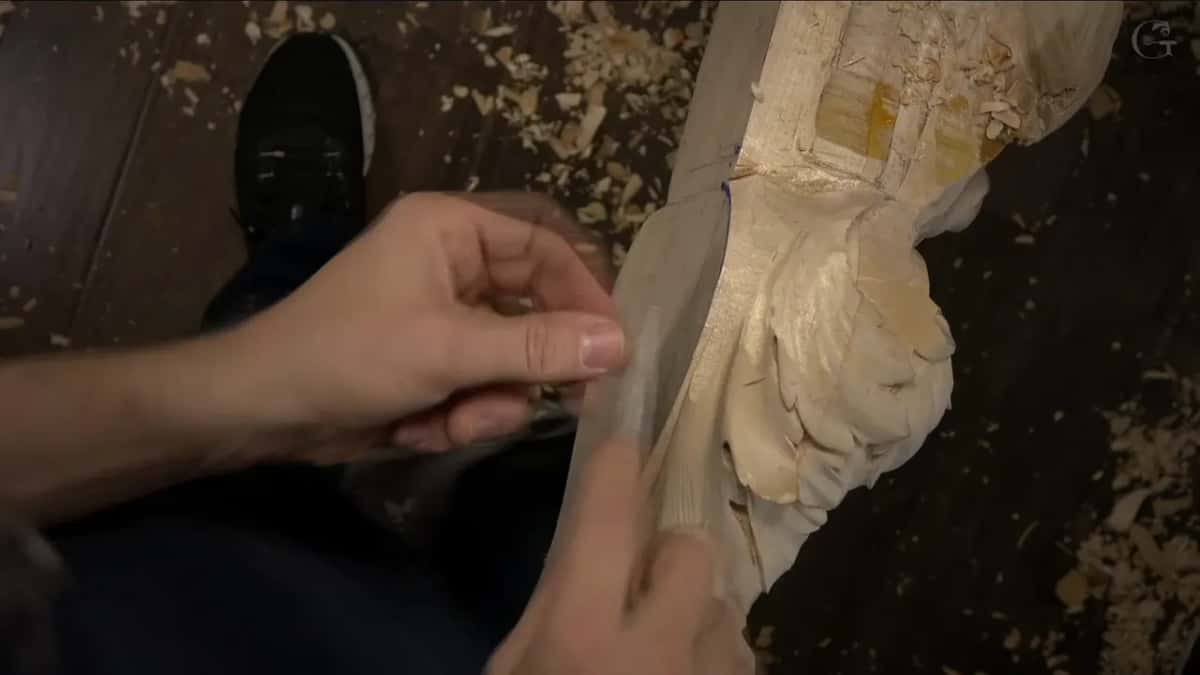 Fingers steady a flat blade against the outer edge, with a sneaker on the floor behind.