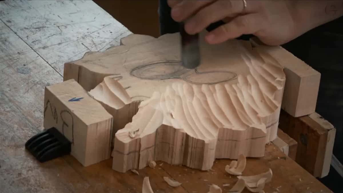 Gouge cutting through a broad band of facets while curled shavings drop onto the bench and pile beside the blank