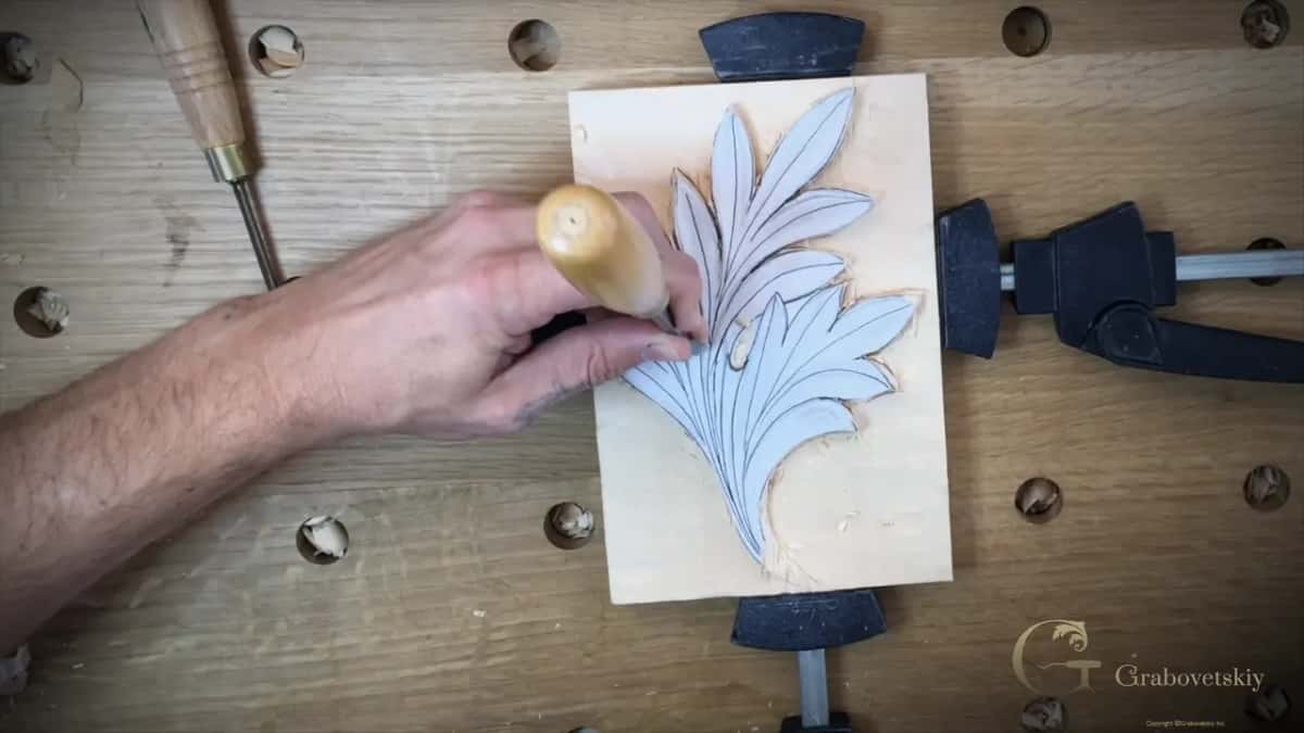 Round mallet head in one hand, a gouge held upright against the leaf in the other.