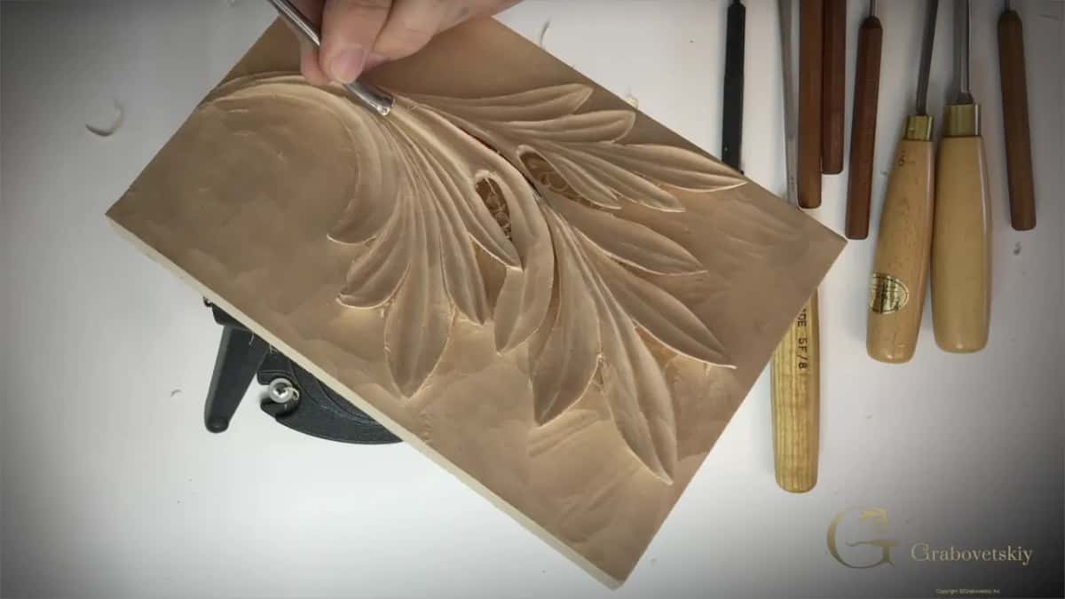 The panel laid flat on the white bench with the leaf cut and a row of gouges beside it.