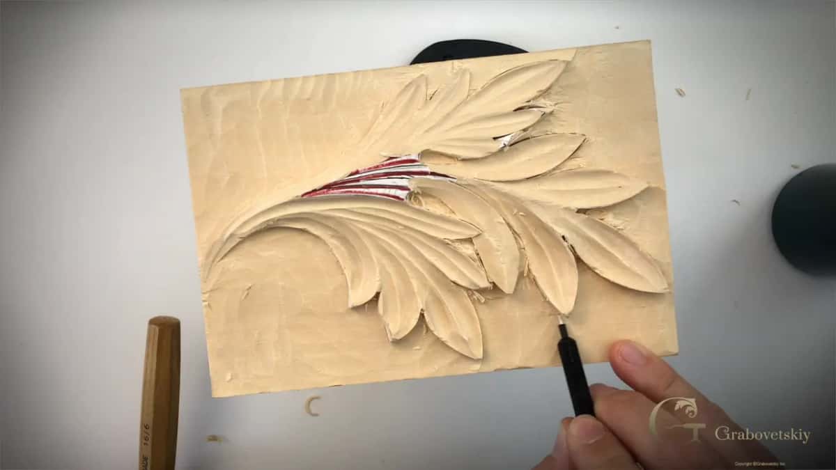 Narrow V tool entering below the lower edge of the leaf while the panel sits on its stand.