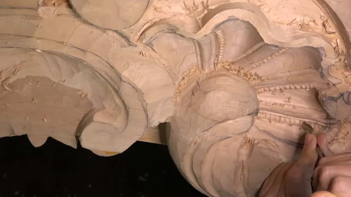 A small tool rounds one bead while the carved ones wait beside it along the same rib.