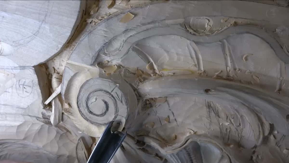 A dark handle steers a gouge along the volute's side.