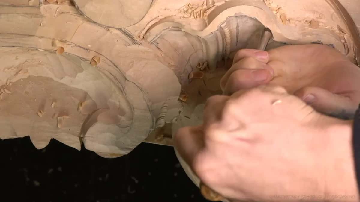 Both hands push one gouge down into the top of the shell hollow while chips gather on the panel.