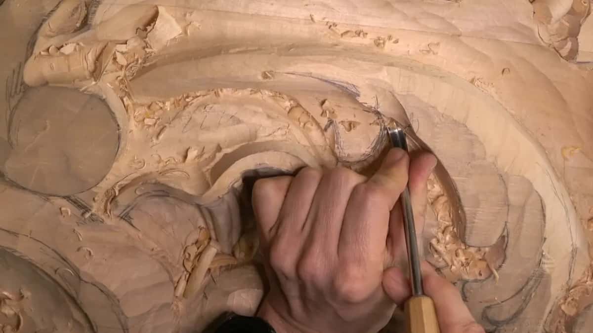 Two hands hold a gouge on the leaf, one near the blade.