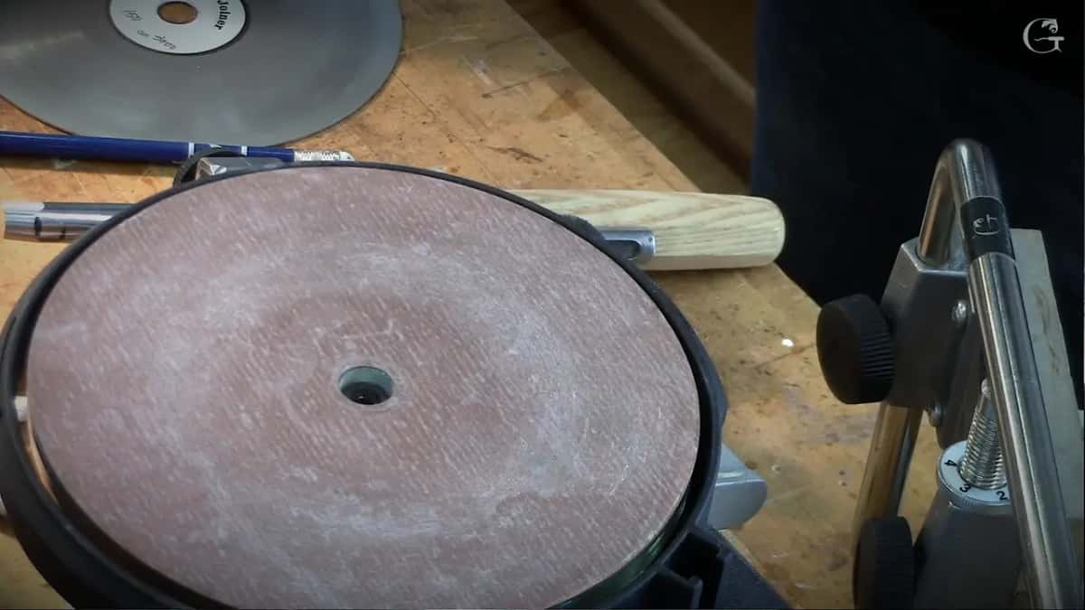Maroon abrasive disc turning on the machine, a tool with a pale turned handle lying behind it on the bench