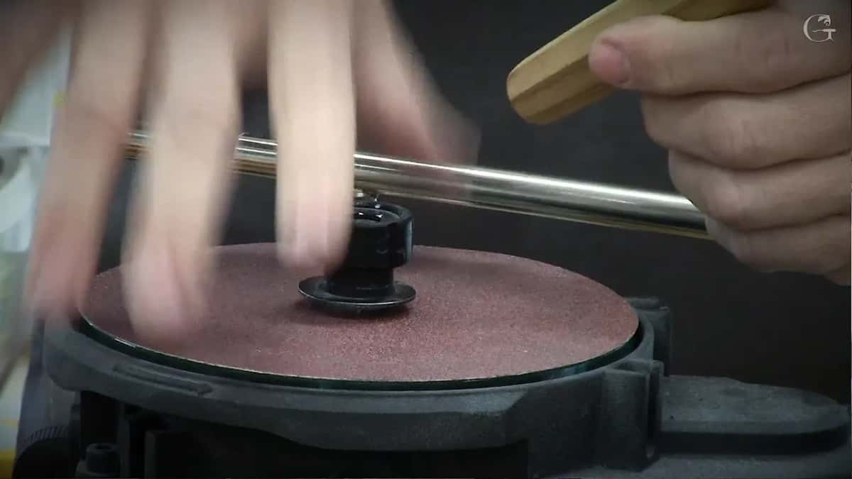 Blurred hand sweeping across a red disc while the other hand steadies a tool at the bar