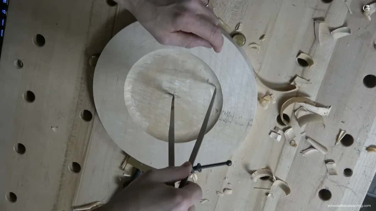 Overhead, the calipers scratch a second circle just inside the edge of the dish.