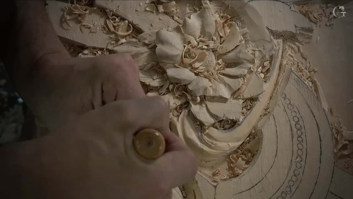 Round end of a handle in the foreground, and the carved flower behind it with chips lying in its petals