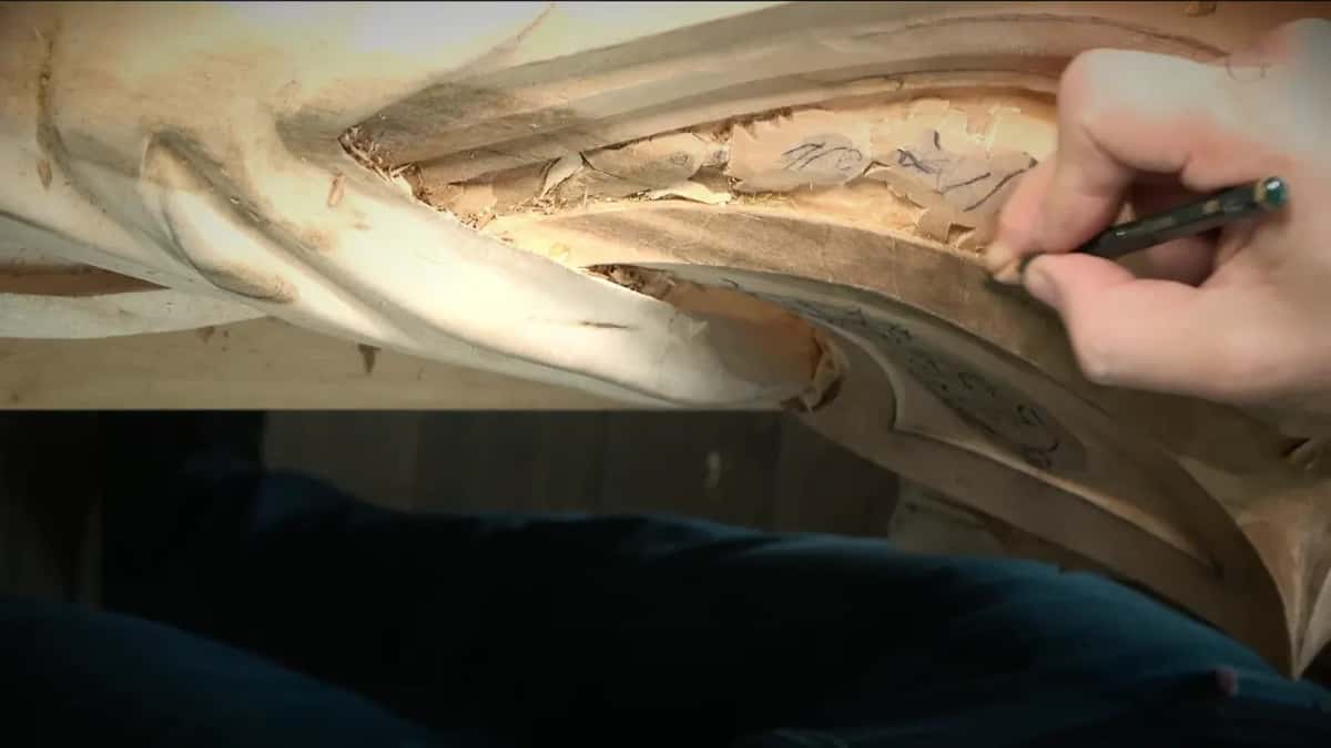 A right hand draws a pencil line along the edge of the panel, next to leaves already sketched inside
