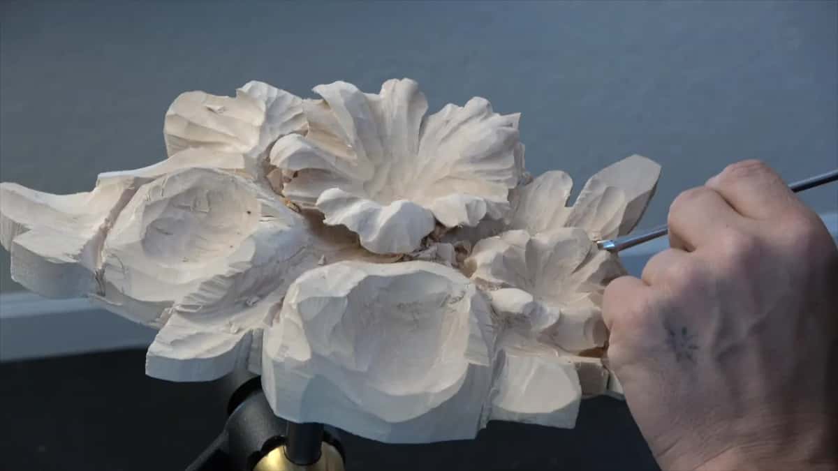 Fist closed round the handle, blade down between two petals, grey wall and skirting behind