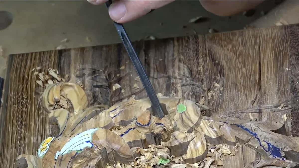 Veiner held upright in the olive, fingertips pinching the top of its shaft while chips pile up below
