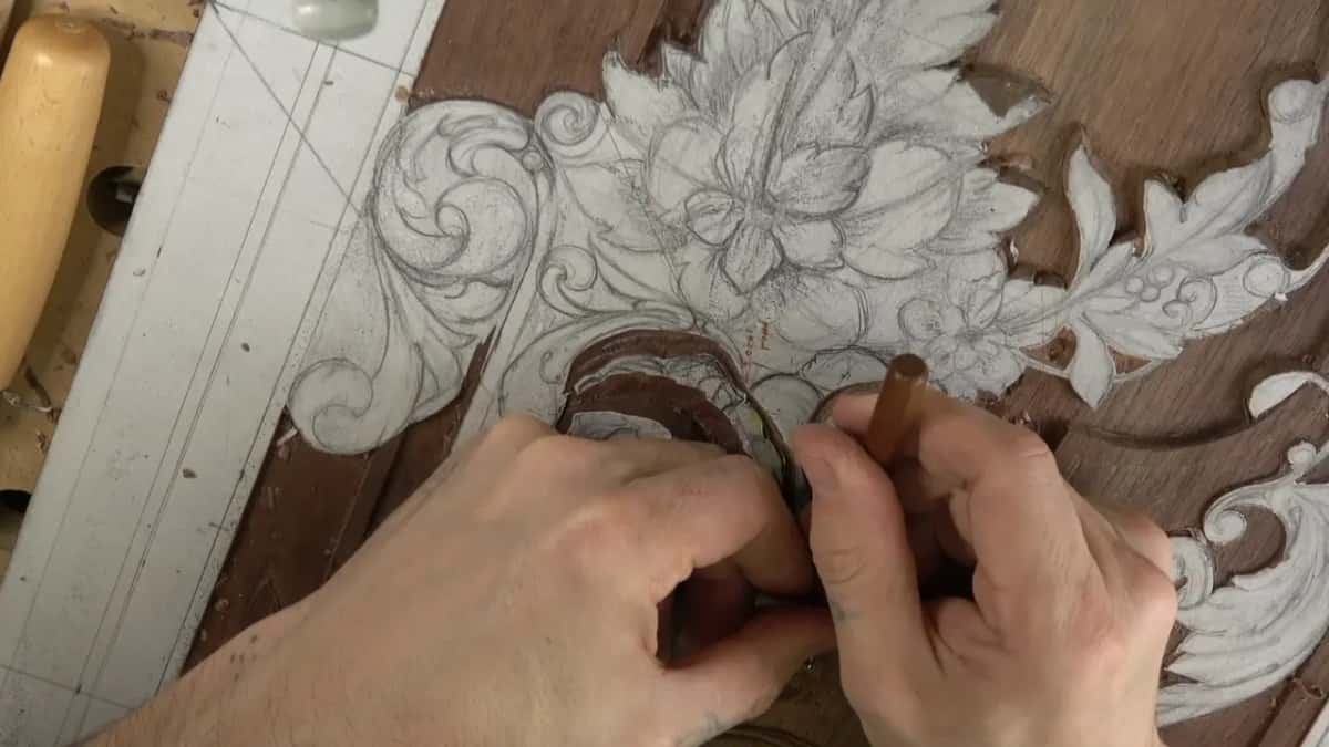 Both hands together over the work, a brown handled gouge upright between them, the drawing still intact above