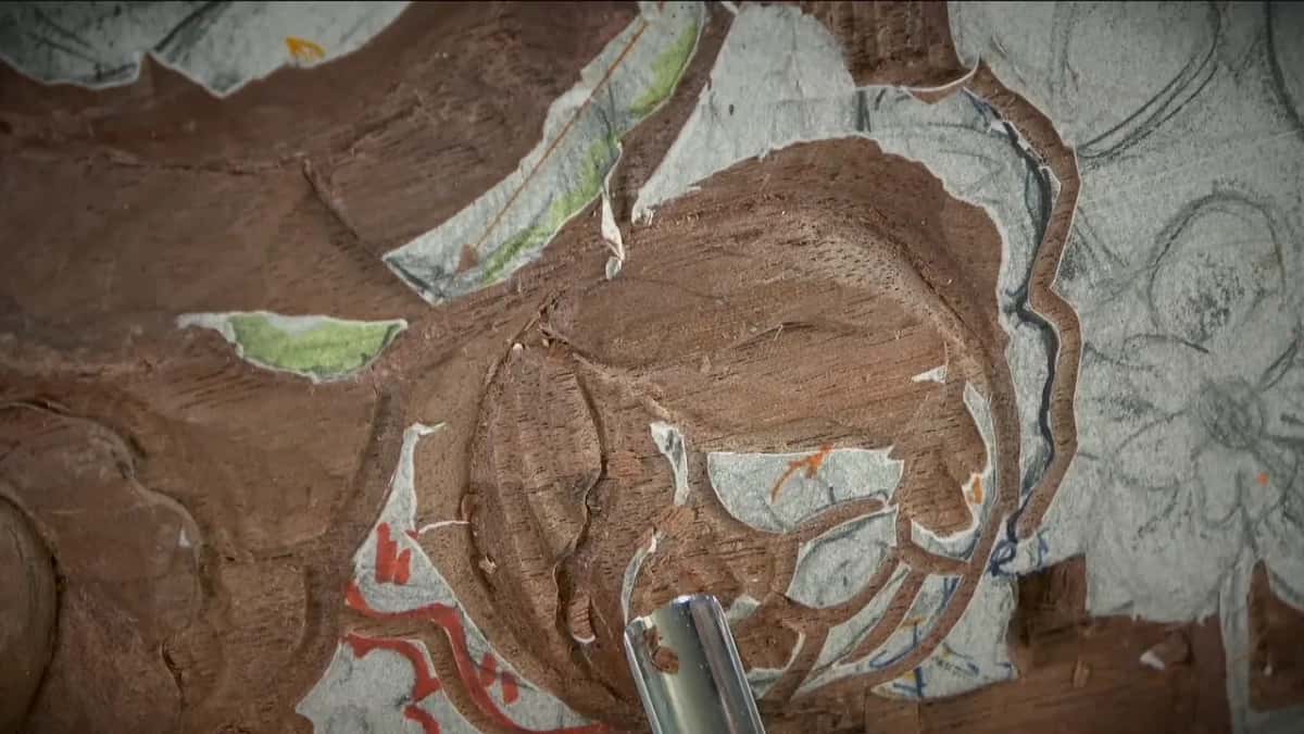 Very close on the carved rose, a steel shaft entering at the bottom, orange and blue drawing all around it