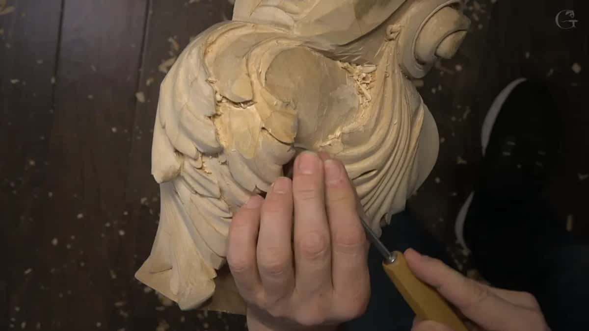 Fingers guide a small tool along the lower edge of the leaves, where fresh chips still sit in the hollow.