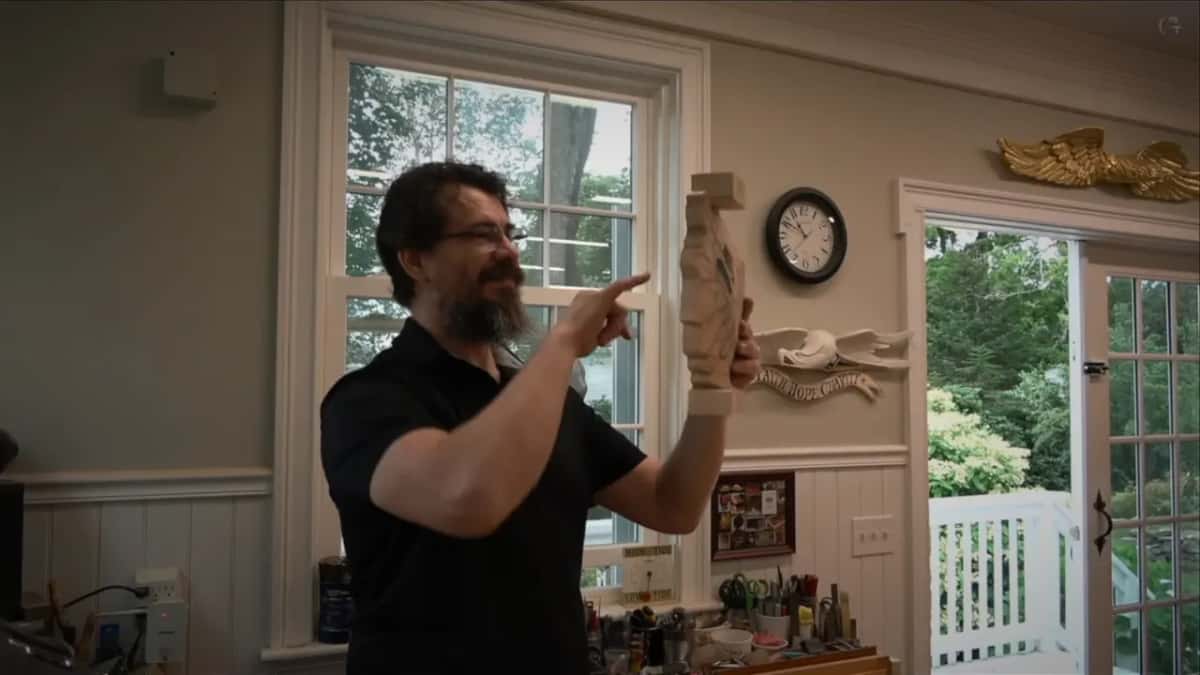 Carved piece held up, a finger pointing at the hole cut right through it