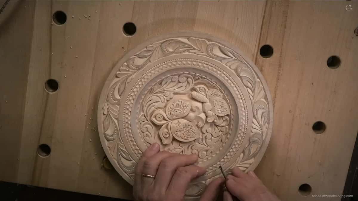 The left hand grips the plate as a tiny tool works near the bottom of the rim