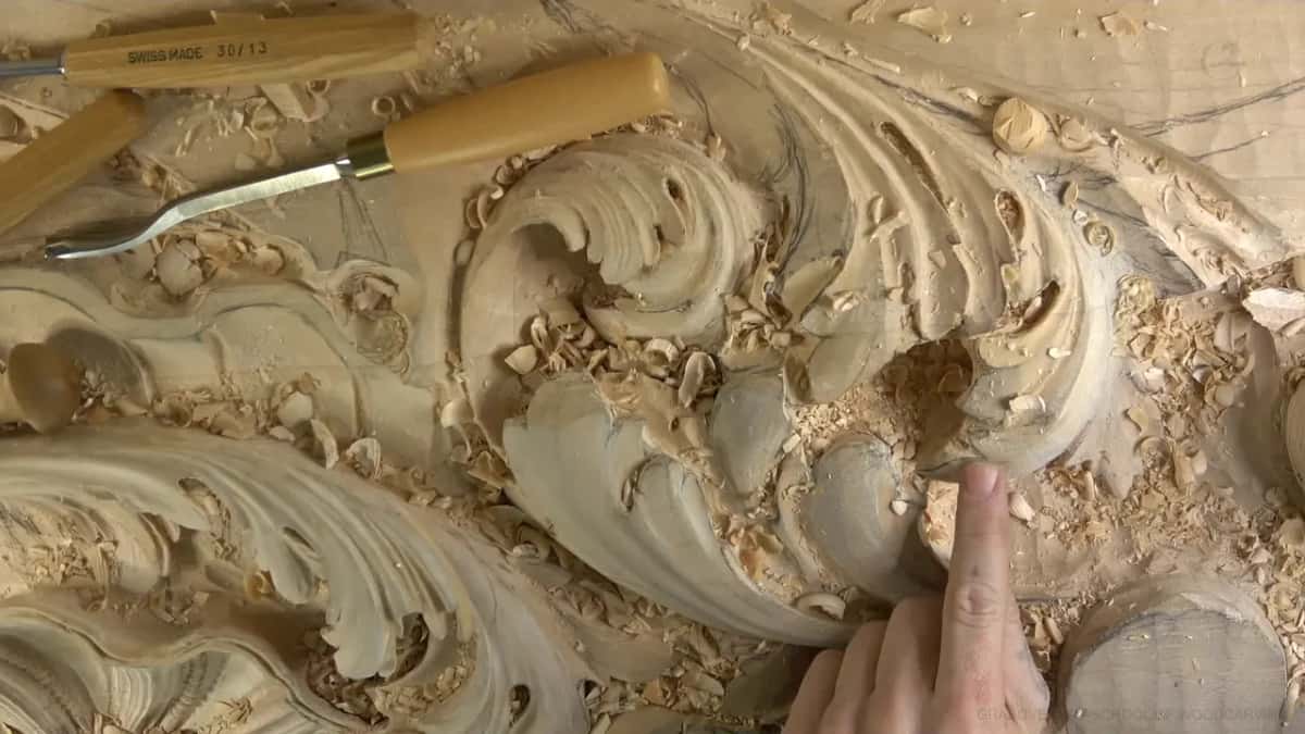 An index finger points to one spot on the right side of the carved leaf.