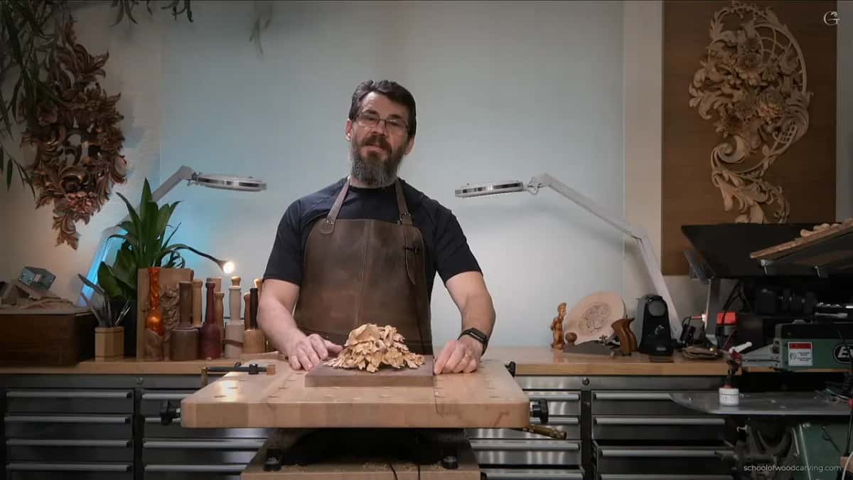 Wide shot of the workshop, the carving flat on its board and his hands resting beside it