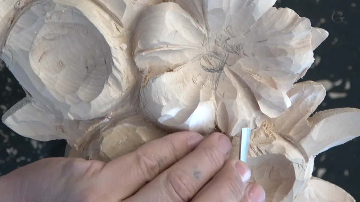 Two fingers guiding a small pale handled tool across a petal, the grip loose enough that nothing is forced
