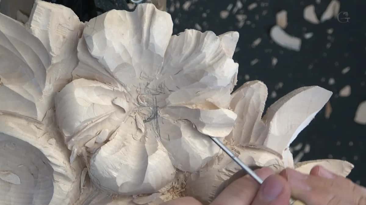 Needle thin blade clearing waste from beneath one petal rim, chips scattered behind