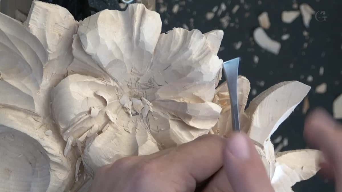 Blade brought in at the right edge of the flower, held so only its tip touches the wood