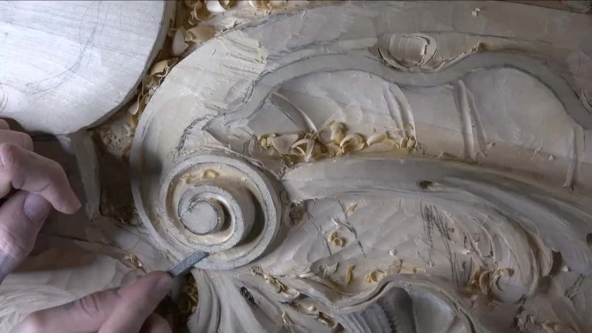 Below the spiral, a metal rasp lies flat on the ring, two hands steadying it from the left.