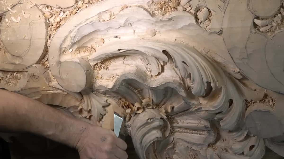 Seen from farther back, a flat skew chisel lowers wood beside the big curling scroll.