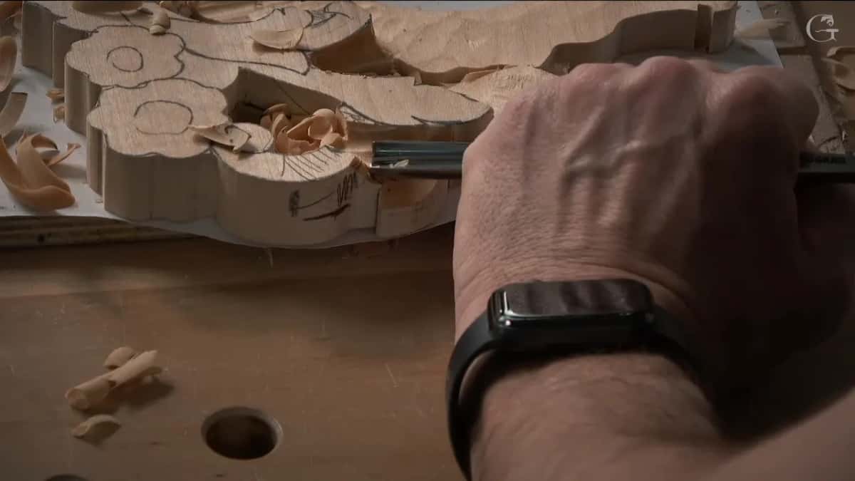 Gouge slicing waste out of the background beside a flower, with shavings gathering across the white board