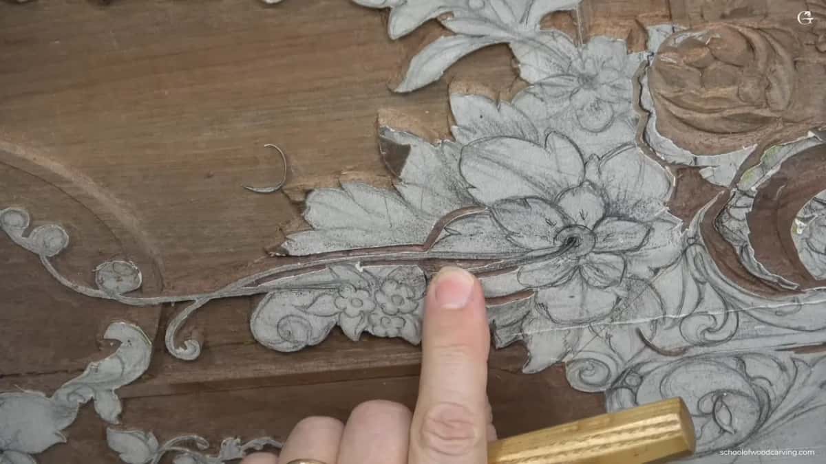 His finger rests on the pencilled bloom, gouge handle waiting below.