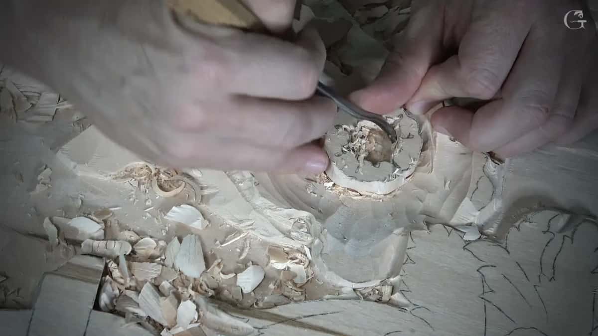 Both hands work a bent tool inside the round, shavings still in the hollow