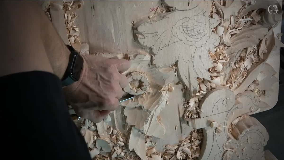 Seen from the side, one hand holds a tool at the flower while chips cover the board