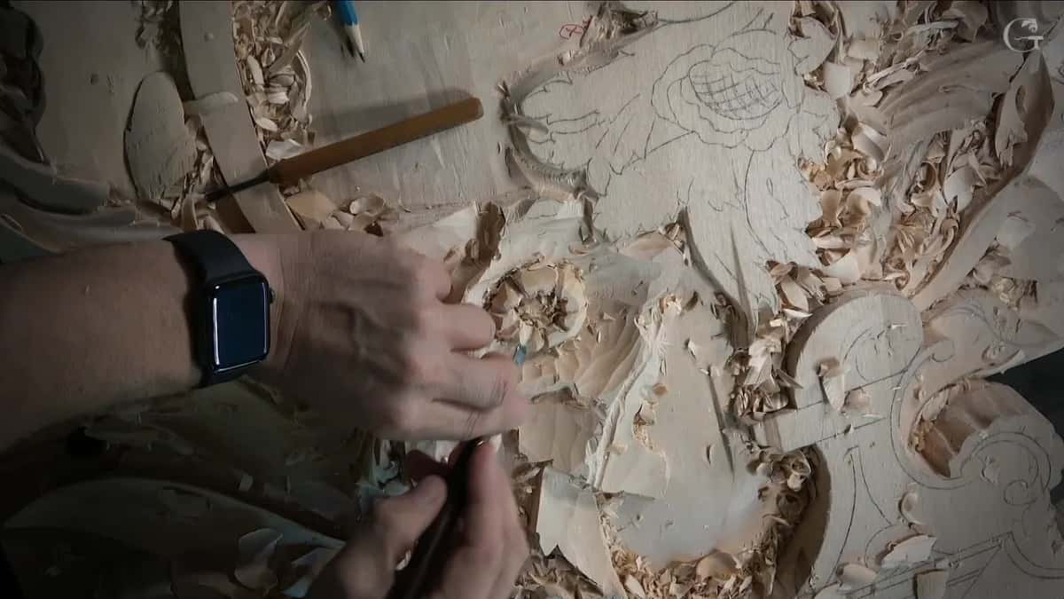 Wrist watch in view as both hands take a small tool around the flower, a gouge resting above