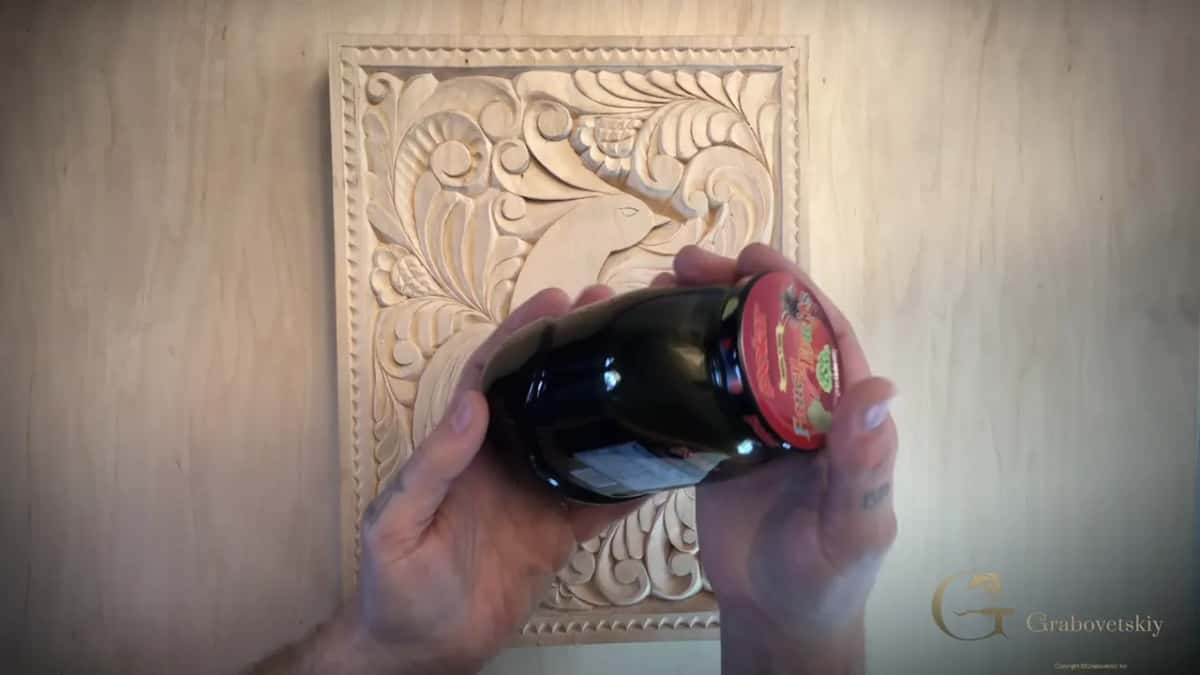 A jar of stain cooked in a kitchen pan, held over the carving it is about to colour.