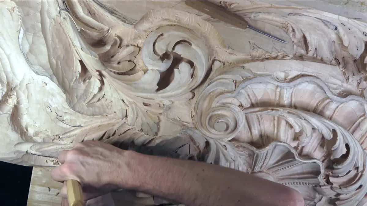 My forearm reaches across the panel, tool tip down among the scrolls, the ribbed shell off to the right.