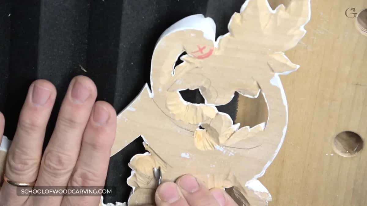 Fingers pinning the flipped carving, a small tool working its back