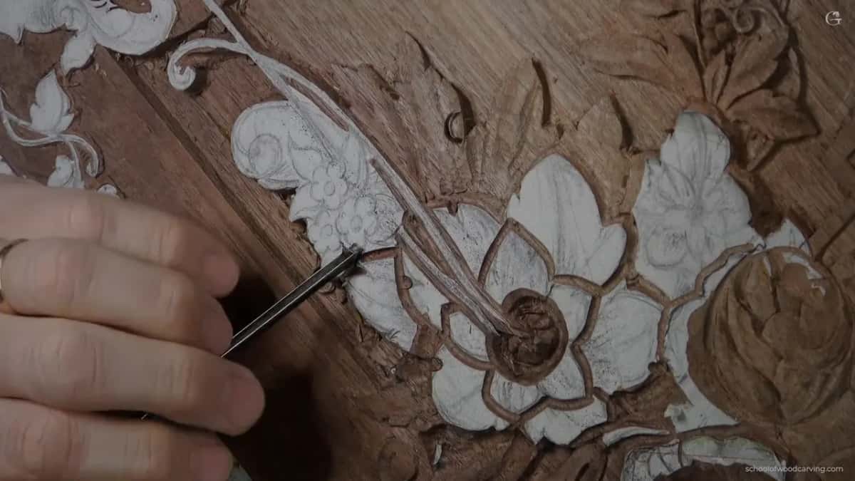 A dark handled antique veiner cutting the outline beside paper petals still glued to the wood.