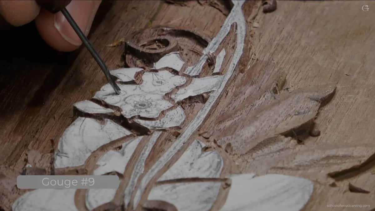 The point of a fine gouge set into the centre of a small carved flower, angled rather than square.