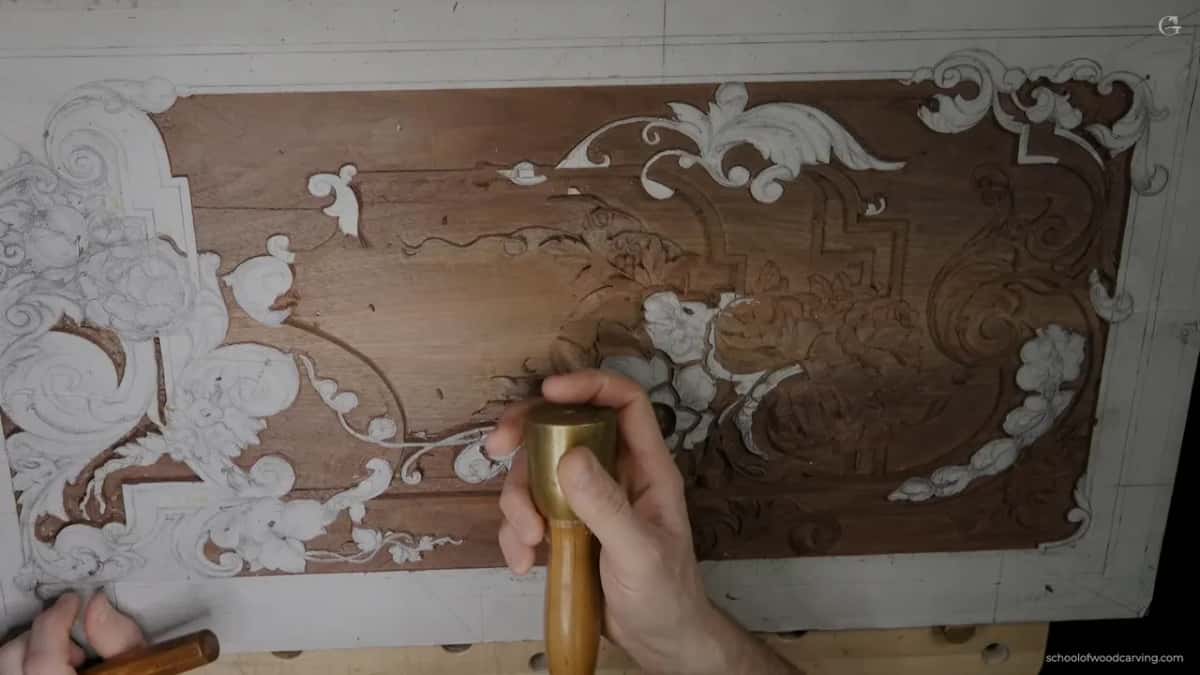 A bronze mallet lying in an open palm above the panel rather than gripped by its handle, the way he keeps control of a tap.