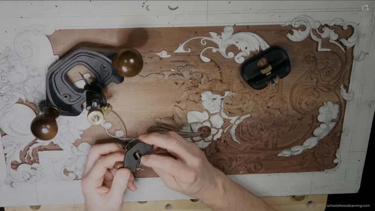 Several router planes of different sizes lying together on the carved panel while a hand reaches for the smallest of them.