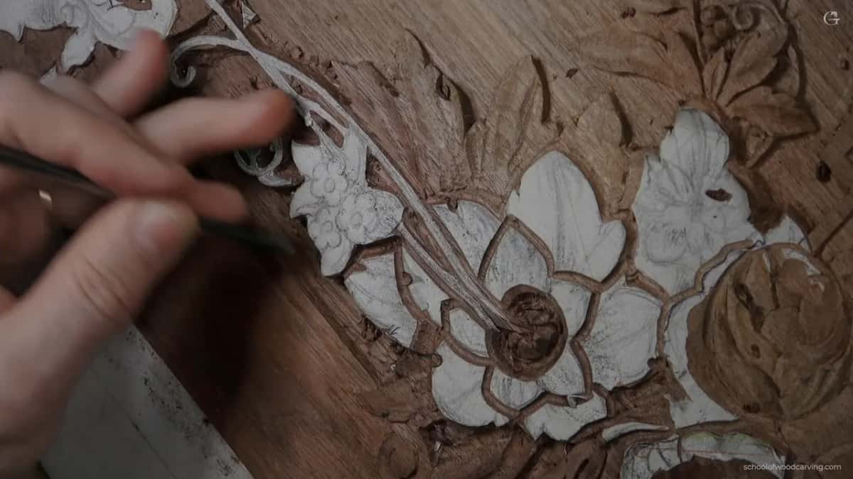 Two hands and a thin blade at a flower whose paper petals are still in place, working where the grain turns awkward.